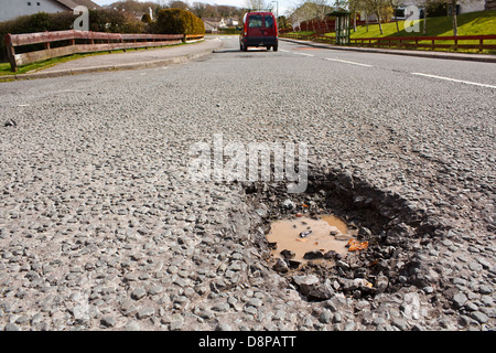 Grande profonda buca un esempio di cattiva manutenzione stradale dovuta alla riduzione locale Consiglio bilanci di riparazione Foto Stock