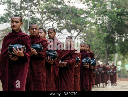 I monaci buddisti raccogliendo elemosine ciotole di cibo al mattino da abitanti di un villaggio vicino a Bagan Birmania Myanmar Foto Stock