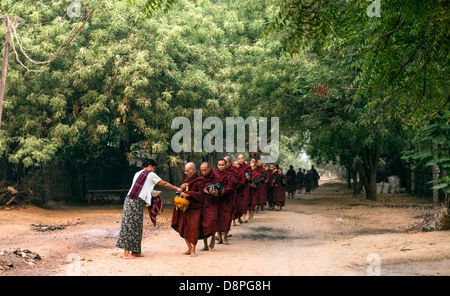 I monaci buddisti raccogliendo elemosine ciotole di cibo al mattino da abitanti di un villaggio vicino a Bagan Birmania Myanmar Foto Stock