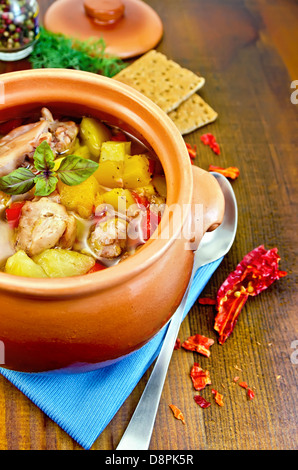 Arrosto con carne di pollo, patate e peperoni in una pentola di creta, igienico, cucchiaio, fette biscottate, aneto su una tavola di legno Foto Stock