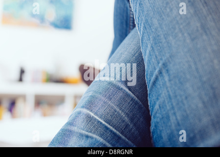 Donna gambe incrociate jeans blu rilassante sul pulmann in una camera bianca Foto Stock