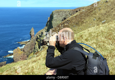 Uomo che guarda al mare attraverso il binocolo con il vecchio uomo di Stoer in background in Sutherland Scozia Scotland Foto Stock