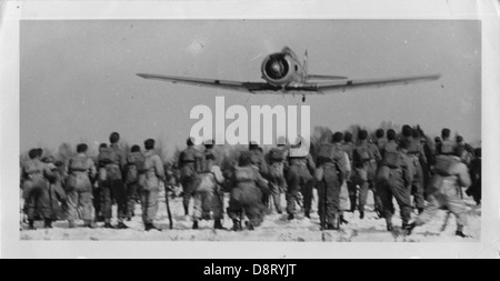 Una fotografia in bianco e nero che mostra un aereo che sorvola le truppe durante la seconda guerra mondiale. L'immagine cattura l'attività aerea comune in tempo di guerra, offrendo uno sguardo alle operazioni militari del periodo. Foto Stock