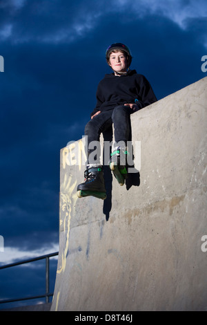 Un giovane skater inline ubicazione sulla cima di un alto muro di cemento in un skate park. Foto Stock