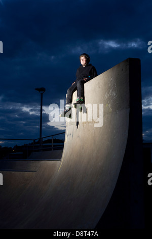 Un giovane skater inline ubicazione sulla cima di un alto muro di cemento in un skate park. Foto Stock