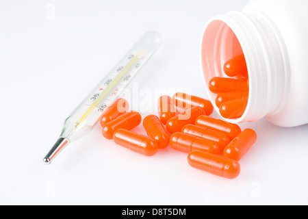 Pillole di arancione e termometro su sfondo bianco Foto Stock