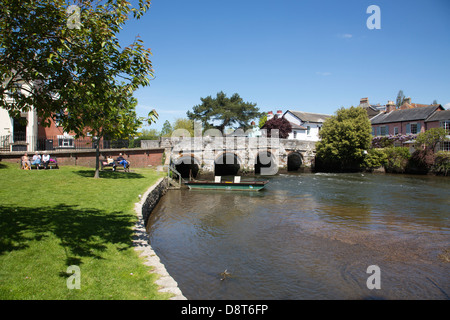 Gente seduta sul lato banca del fiume Avon che gira sotto Bridge Street, nella città di Christchurch, Dorset, England, Regno Unito Foto Stock