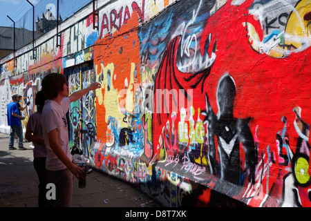 Ragazzi con bombolette spray in vicolo spruzzatura coloratissimo graffito sulla parete dell'edificio della città Foto Stock