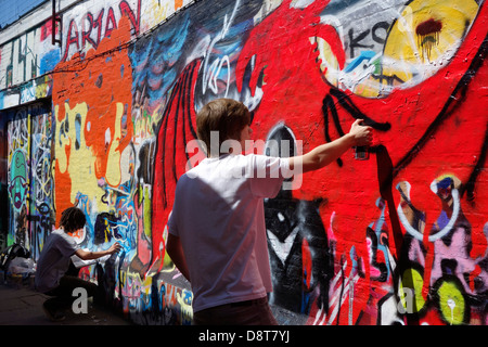 Ragazzi con bombolette spray in vicolo spruzzatura coloratissimo graffito sulla parete dell'edificio della città Foto Stock