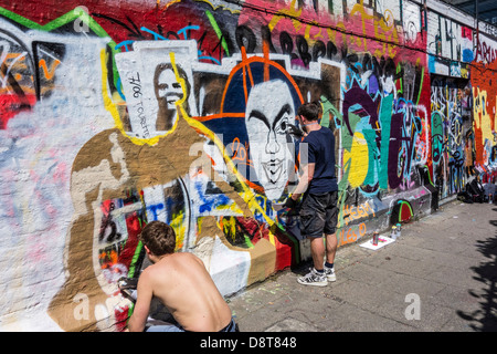 Ragazzi con bombolette spray in vicolo spruzzatura coloratissimo graffito sulla parete dell'edificio della città Foto Stock