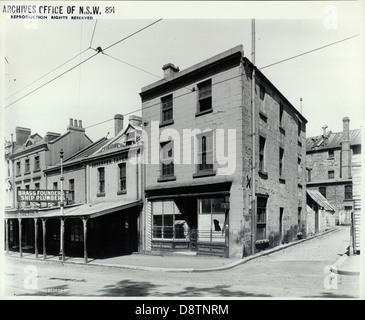 L'Observer Tavern, situata in George Street a The Rocks, Sydney, è uno storico pub che ha svolto un ruolo importante nella vita sociale della zona. La fotografia d'archivio in bianco e nero cattura l'iconica struttura, che era un punto fermo del quartiere Rocks. L'immagine mostra l'architettura del pub e le strade circostanti, offrendo uno sguardo sulla storia dei primi sviluppi di Sydney e della vita della comunità. Foto Stock