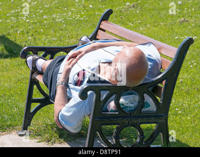 Uomo dorme sul banco a inizio estate sole, Whitburn, North East England, Regno Unito Foto Stock