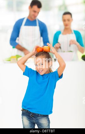 Bambina divertendosi con pomodori mentre i suoi genitori la cottura in cucina Foto Stock