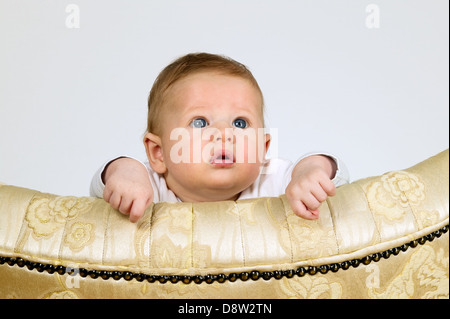 Baby boy è guardare attraverso una parte superiore della sedia vintage Foto Stock