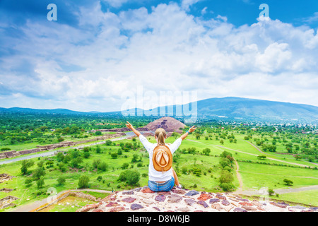 Lato posteriore della donna seduta con alzata fino a mani sulla cima delle montagne e godersi la vista del messicano piramide di Teotihuacan Foto Stock