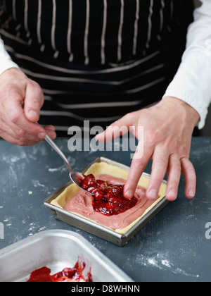 Ponendo la confettura di fragole al centro della torta sulla crema pasticcera Foto Stock