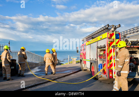 I vigili del fuoco di mettere un piccolo incendio in una cucciolata bin al mare tramite un lungo tubo antincendio da un motore Fire Foto Stock