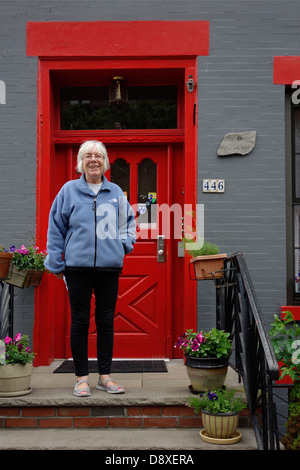 Senior donna in piedi sui gradini di una casa Foto Stock