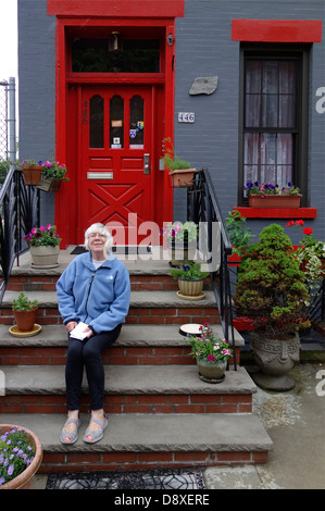 Senior donna seduta sui gradini di una casa Foto Stock