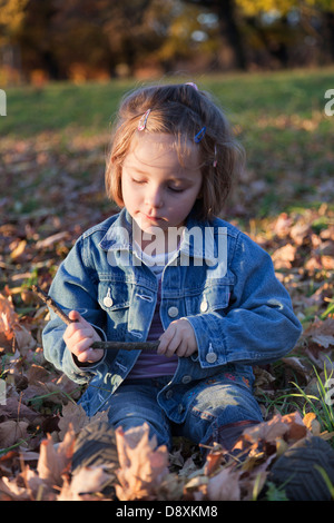 Quattro anni di ragazza seduta in foglie di autunno Foto Stock
