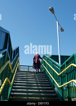 Donna anziana che lotta sul ponte pedonale sopra la linea ferroviaria in Sandbach Cheshire Regno Unito Foto Stock