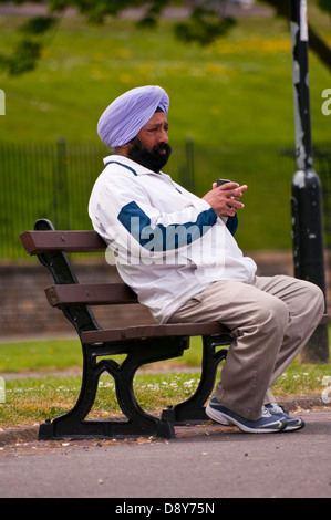 La religione sikh uomo seduto fuori su un banco che indossa un turbante Foto Stock