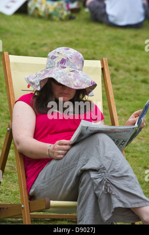 Donna che indossa un floppy hat seduto nella sedia sdraio rivista di lettura a Hay Festival 2013 Hay on Wye Powys Wales UK Foto Stock