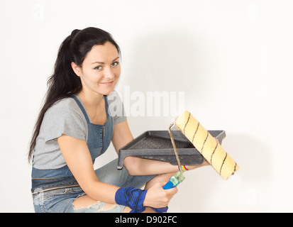 Sorridente giovane donna in possesso di un vassoio di vernice e il rullo nelle sue mani come lei si prepara ad iniziare la pittura la sua casa Foto Stock