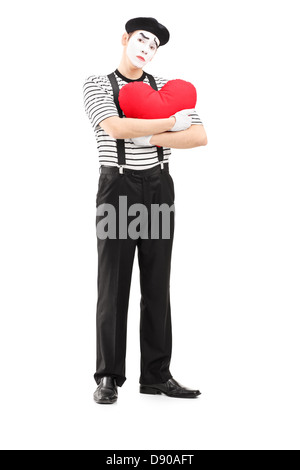 A piena lunghezza Ritratto di un triste artista mime tenendo un cuore rosso isolato su sfondo bianco Foto Stock