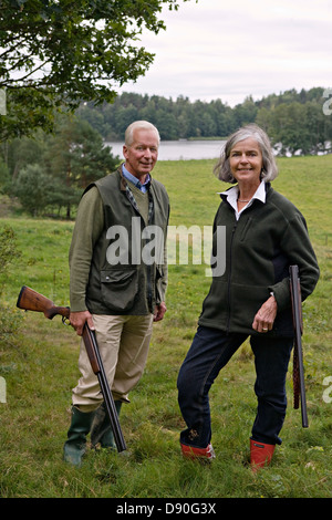 Coppia senior fucile tenuta in piedi sull'erba, sorridente Foto Stock