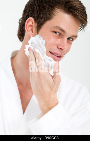 Bel giovane Applicare schiuma da barba sulla faccia nella stanza da bagno Foto Stock
