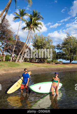 Coppia con stand-up paddleboard e tavole da surf a Launiupoko stato parco lungo il tragitto appena a sud di Lahaina, Maui Foto Stock