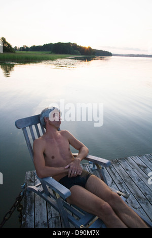 L'uomo rilassarsi sui lettini prendisole sul molo Foto Stock