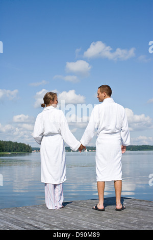 Coppia giovane in accappatoio in piedi sul molo, tenendo le mani Foto Stock