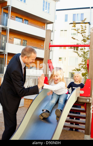 Padre e figlie giocando sulla diapositiva Foto Stock