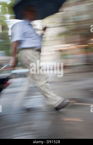 Uomo che cammina con ombrellone, offuscata Foto Stock