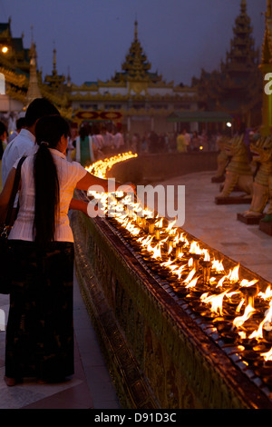 Come il crepuscolo scende i visitatori della Shwedagon pagoda luce complessi i votives in un anello attorno alla centrale (Zedi stupa), Yangon, Birmania Foto Stock