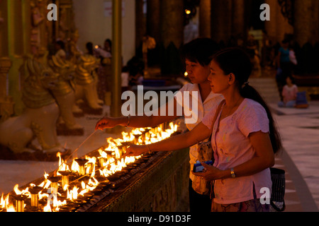 Come il crepuscolo scende i visitatori della Shwedagon pagoda luce complessi i votives in un anello attorno alla centrale (Zedi stupa), Yangon, Birmania Foto Stock