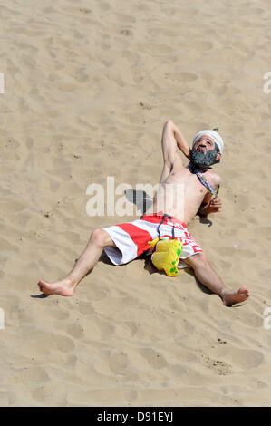 Porthcawl, South Wales, Regno Unito 8 Giugno 2013. Il clima caldo attrae folle di Porthcawl beach in Galles del sud su uno dei giorni più caldi dell'anno. Un giovane uomo sunbathes con un Osama Bin Laden sulla maschera a Porthcawl beach. Credito: Matteo Horwood/Alamy Live News Foto Stock