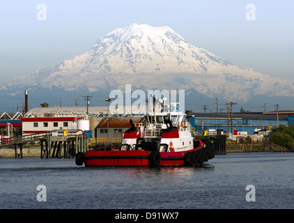 Un rimorchiatore che restituisce al molo dopo la guida di una nave portacontainer in mare mt. Rainier in background Foto Stock