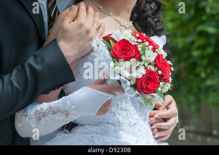 Lo sposo abbraccia la sposa con un bouquet in mano Foto Stock