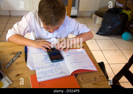 Tredici ragazzo di 13 anni matematica facendo i compiti sul tavolo da cucina con un calcolatore elettronico Foto Stock