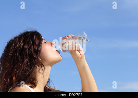 Profilo di una donna di bere acqua da una bottiglia di plastica con un cielo blu in background Foto Stock