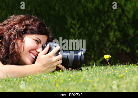 Profilo di una bella donna di prendere una fotografia macro di un fiore sul prato di un parco Foto Stock