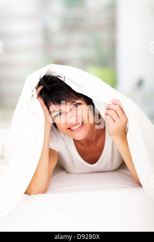 Divertimento donna di mezza età che giace sotto il piumone ridere Foto Stock