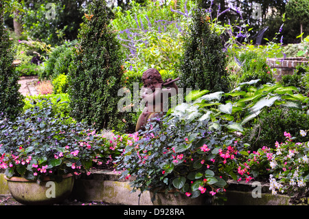 Piccola statua in ceramica di un fauno suonare il flauto in tra fiori colorati Foto Stock