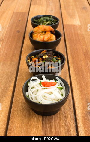 Cibo asiatico composta con quattro coppe nero con gamberetti, riso tagliatelle, kale (cavolo verde) e verdure fritte. Foto Stock