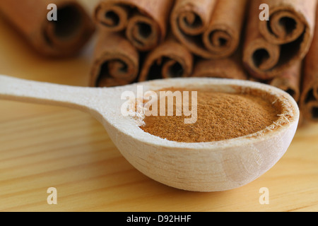 La cannella in polvere il cucchiaio di legno con bastoncini di cannella in background Foto Stock