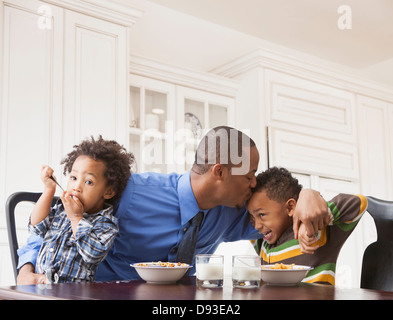 Padre baciare figli al tavolo per la colazione Foto Stock