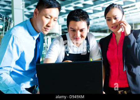 Lavoratore o manager di produzione e per il servizio di assistenza clienti, guarda su un computer portatile in una fabbrica tessile e la guida sul telefono Foto Stock